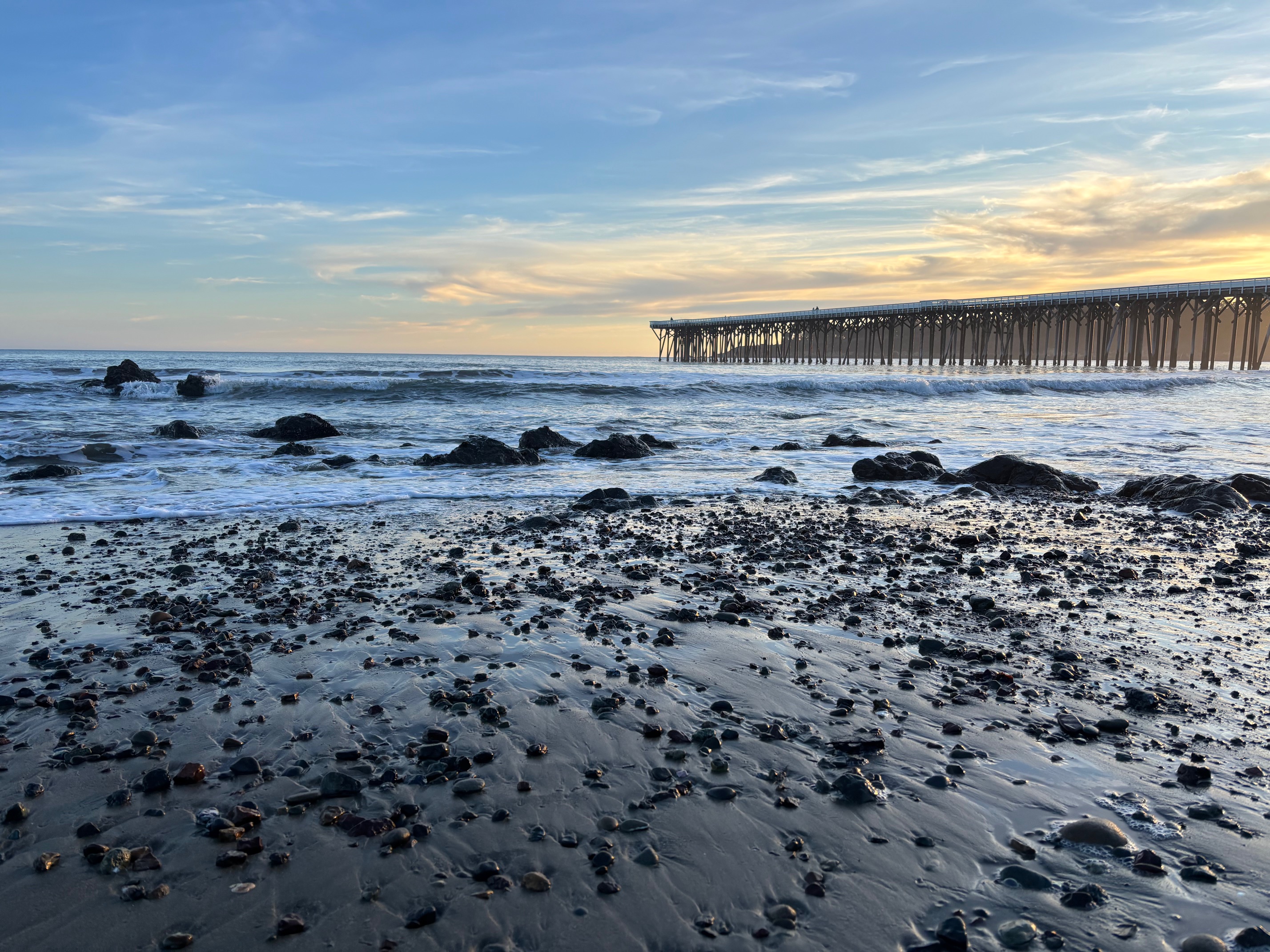 Rocks in the foreground on a beach with a wooden pier in the background